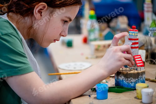 Preview: cute teen girl at a master class making a DIY wooden lighthouse made of wood, exhibition of crafts