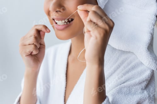 Preview: cropped view of smiling young african american woman in bathrobe flossing teeth in bathroom