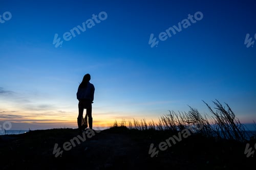 Preview: Silhouette of woman stand at the top of the mountain in the evening