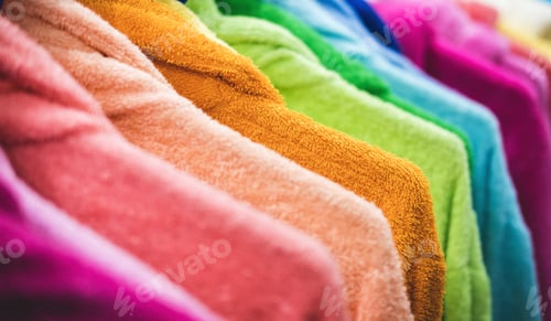 Preview: Multi-colored terry robes hanging in a row on hanger. Creative presentation of clothing for sale.