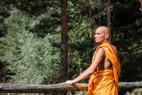 Preview: man in buddhist traditional clothes standing near wooden fence in forest and looking away
