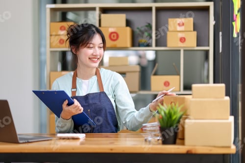 Preview: Startup SME small business entrepreneur of freelance Asian woman wearing apron using laptop and box