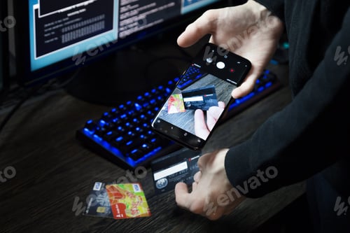 Preview: A hacker sits in front of a computer and scans the codes of payment cards using his phone
