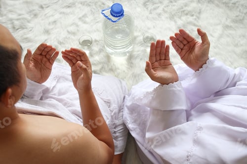 Preview: Close up shot of muslim couple wearing white ihram clothes, praying before drinking zam zam water.