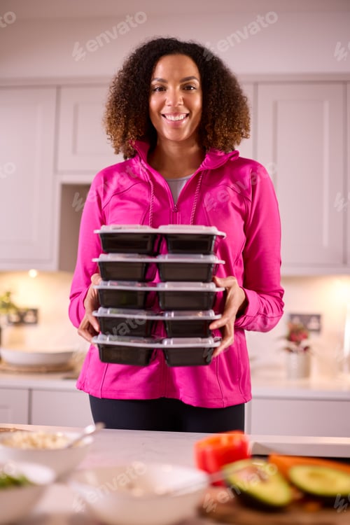 Preview: Portrait Of Woman In Kitchen Wearing Fitness Clothing Making Batch Of Healthy Meals For Freezer