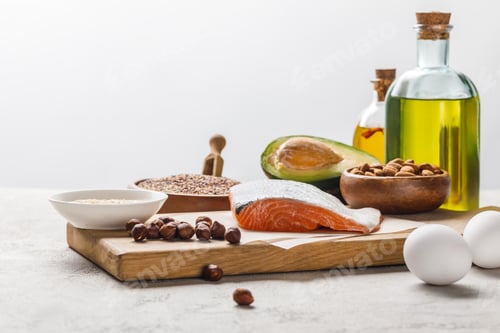 Preview: fresh raw salmon, nuts, eggs and avocado on wooden chopping board near oil isolated on grey,