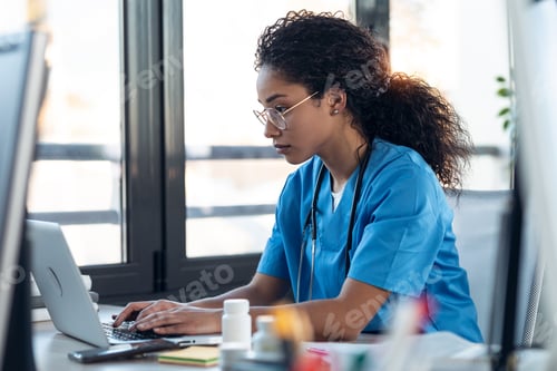Preview: Attractive young afro female doctor talking working with her computer in the consultation.