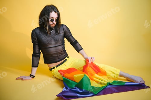 Preview: Gay man wearing bright pink top hold rainbow striped flag isolated on colored background