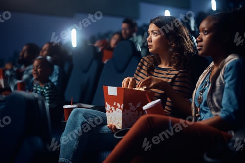 Preview: Young woman eating popcorn while watching sad movie in cinema.