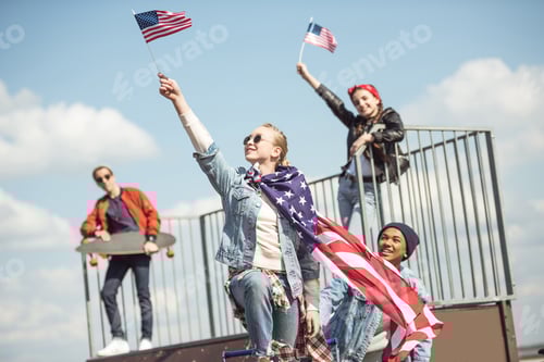 Preview: Teenagers group having fun together and waving american flags at skateboard park