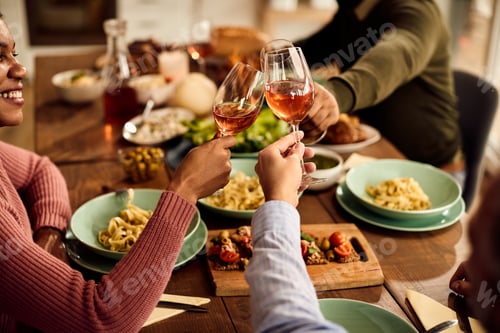 Preview: Close-up of friends toasting with wine during lunch at dining table.