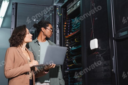 Preview: young interracial engineers with laptop making diagnostics of server in data center