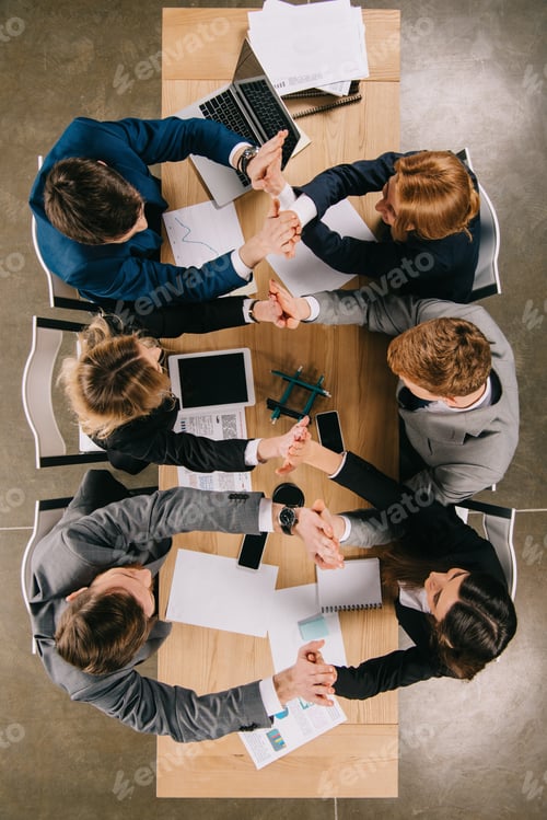 Preview: Top view of businesspeople holding hands of each other while sitting at table in office