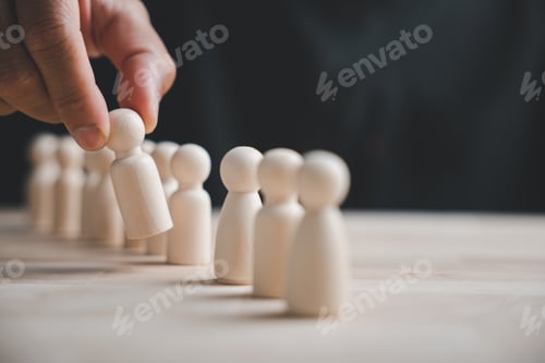 Preview: Hand picking out a wooden figure from a row of figures on a table.