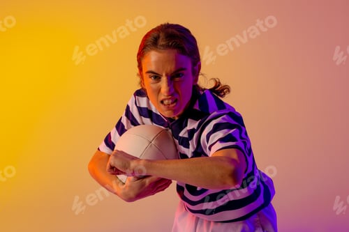 Preview: Portrait of caucasian female rugby player with rugby ball over neon pink lighting