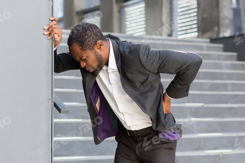 Preview: Overtired and sick african american man outside office building has severe back pain, businessman