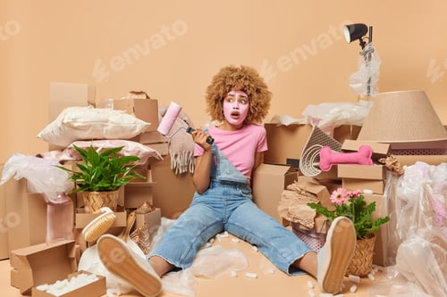 Preview: Photo of tired woman holds paint roller tired of redecorating room relocates to new apartment applie