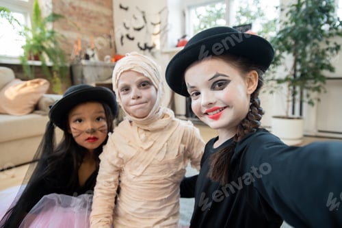 Preview: Happy halloween girl making selfie with two kids in costumes
