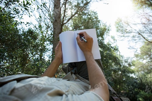 Preview: Man lying in hammock writing in notebook, partial view
