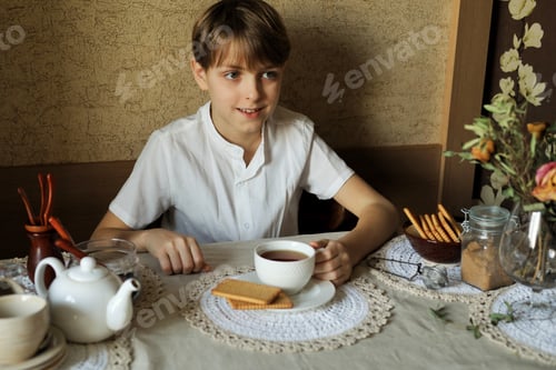 Preview: A charming boy of 10 years old sits at an elegantly decorated table and drinking tea with cookies