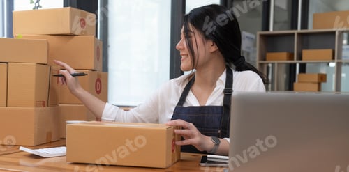 Preview: Smiling entrepreneur checking order on delivery box on work desk at home