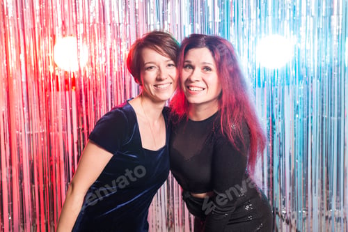 Preview: Portrait of two attractive happy women in evening dresses hugging and looking at camera isolated