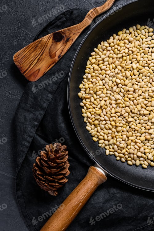 Preview: Roasted pine nuts in a frying pan. Black background. Top view