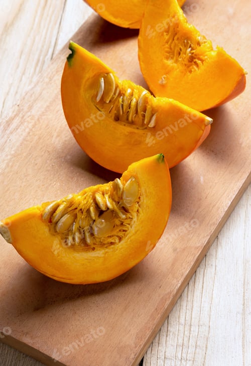 Preview: Yellow pumpkin slices on cutting board. Fresh cut squashes on wooden table. Place for text.