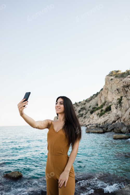 Preview: Stylish woman taking selfie on beach