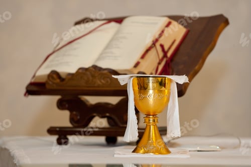 Preview: Golden chalice displayed on a white altar cloth with an open bible