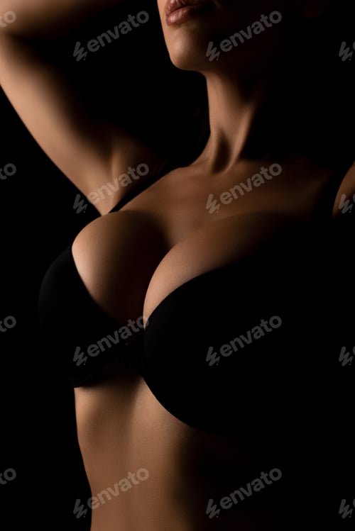 Preview: cropped view of girl with big breasts posing with raised hands isolated on black