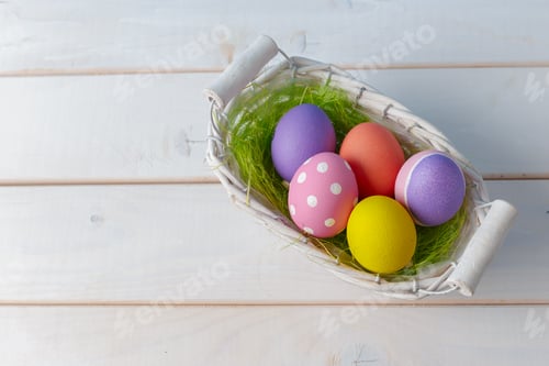 Preview: Colorful Easter eggs in a decorative basket filled with green grass on a wooden table