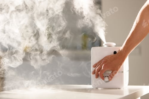 Preview: Hand turn on aroma oil diffuser on the table at home, steam from air humidifier