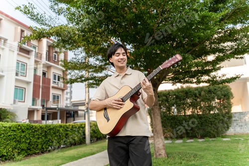 Preview: Asian handsome man musician playing an acoustic guitar in the garden.