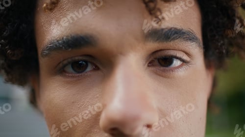 Preview: Brown eyes man looking camera outdoors extreme closeup. Curly teen staring lens