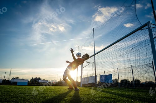 Preview: Football player is training at the field on a sunset background.