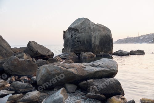 Preview: Serene lake view with a massive rock formation in the foreground