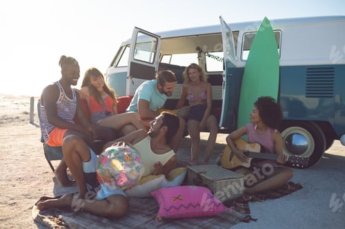 Preview: Front view of happy group of diverse friends having fun near camper van at beach