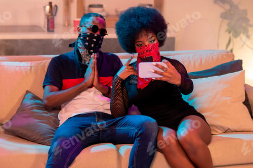 Preview: Young African man in face bandana sitting next to girl with nikab making selfie