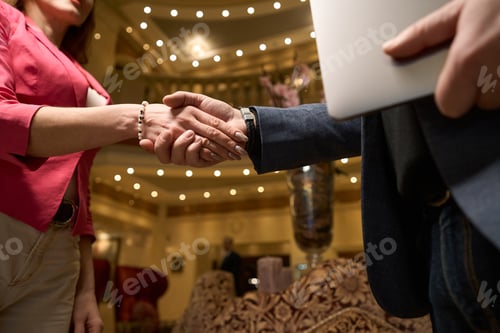 Preview: Handshake of man and woman in lobby of large hotel