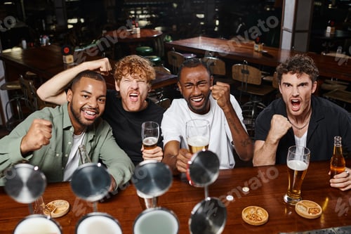 Preview: four excited multiethnic football fans holding glasses of beer and cheering, male friends in bar