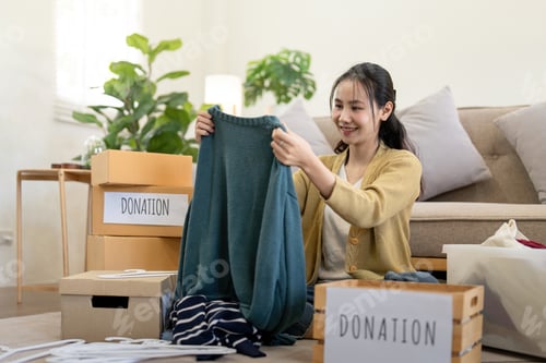 Preview: Woman asian holding donation box full with clothes and select clothes. Concept of donation and