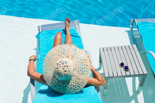 Preview: Woman in hat relaxing at the pool with pina colada cocktail