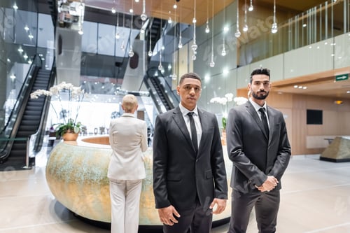 Preview: interracial bodyguards looking at camera near senior business lady checking in at hotel reception