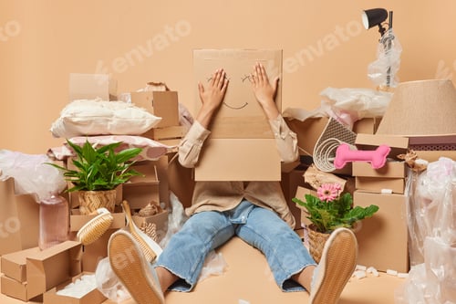 Preview: Unrecognizable woman covers head with cardboard box poses on floor surrounded by personal belongings