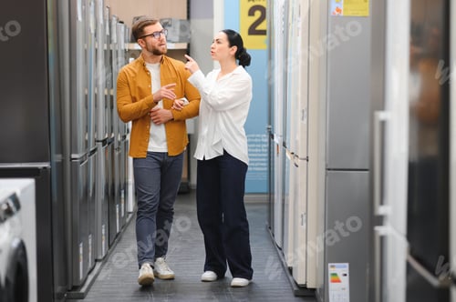 Preview: Young couple, satisfied customers choosing fridge in appliances store
