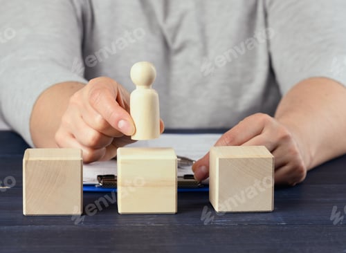 Preview: Female hand holds a wooden figurine of a man and puts on a cube