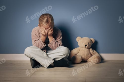 Preview: Sad little girl with toy bear crying near blue wall indoors
