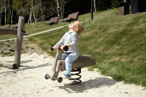 Preview: Little caucasian blond boy playing on kids playground in a sunny autumn day