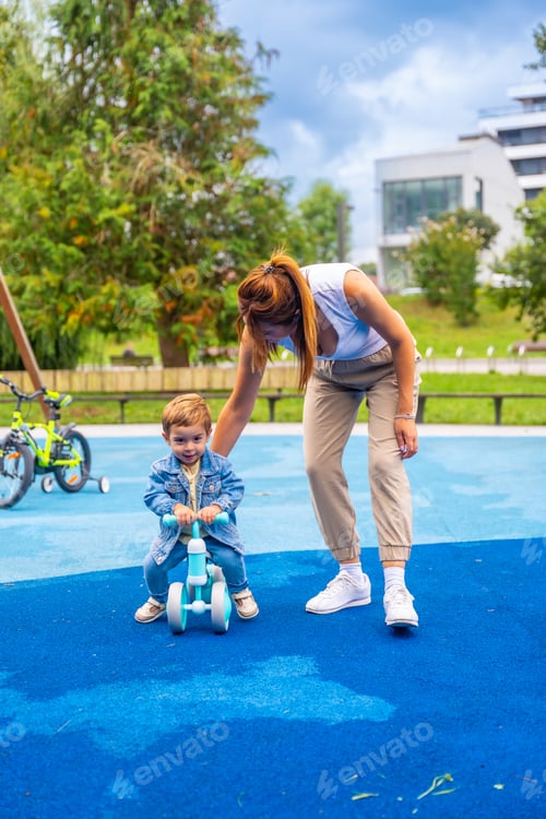 Preview: Mother helping son riding balance bike in playground